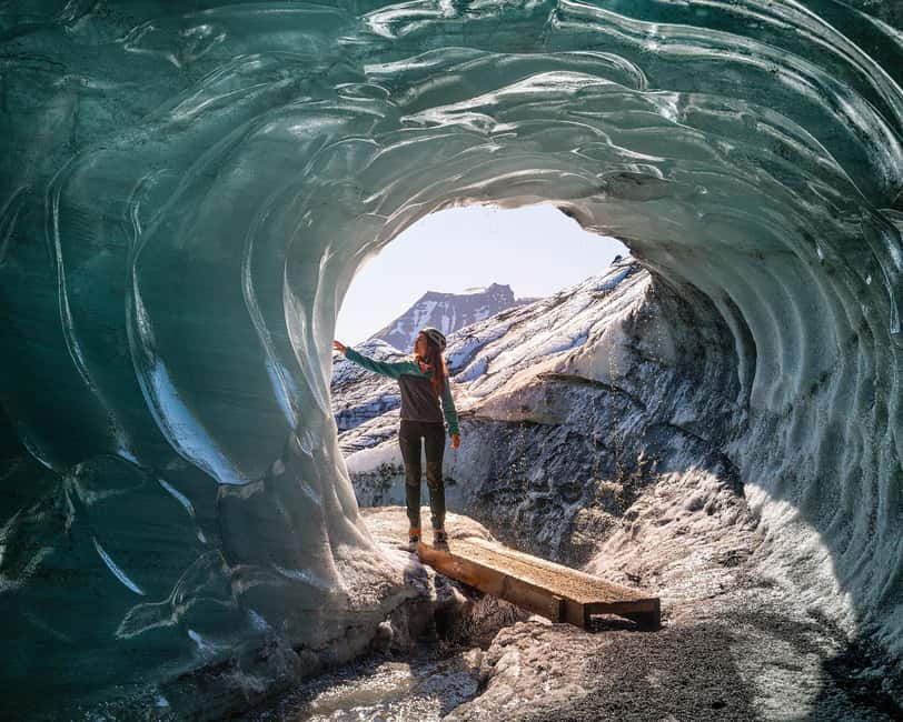 A guide standing under the mouth of a blue ice cave beneath Katla